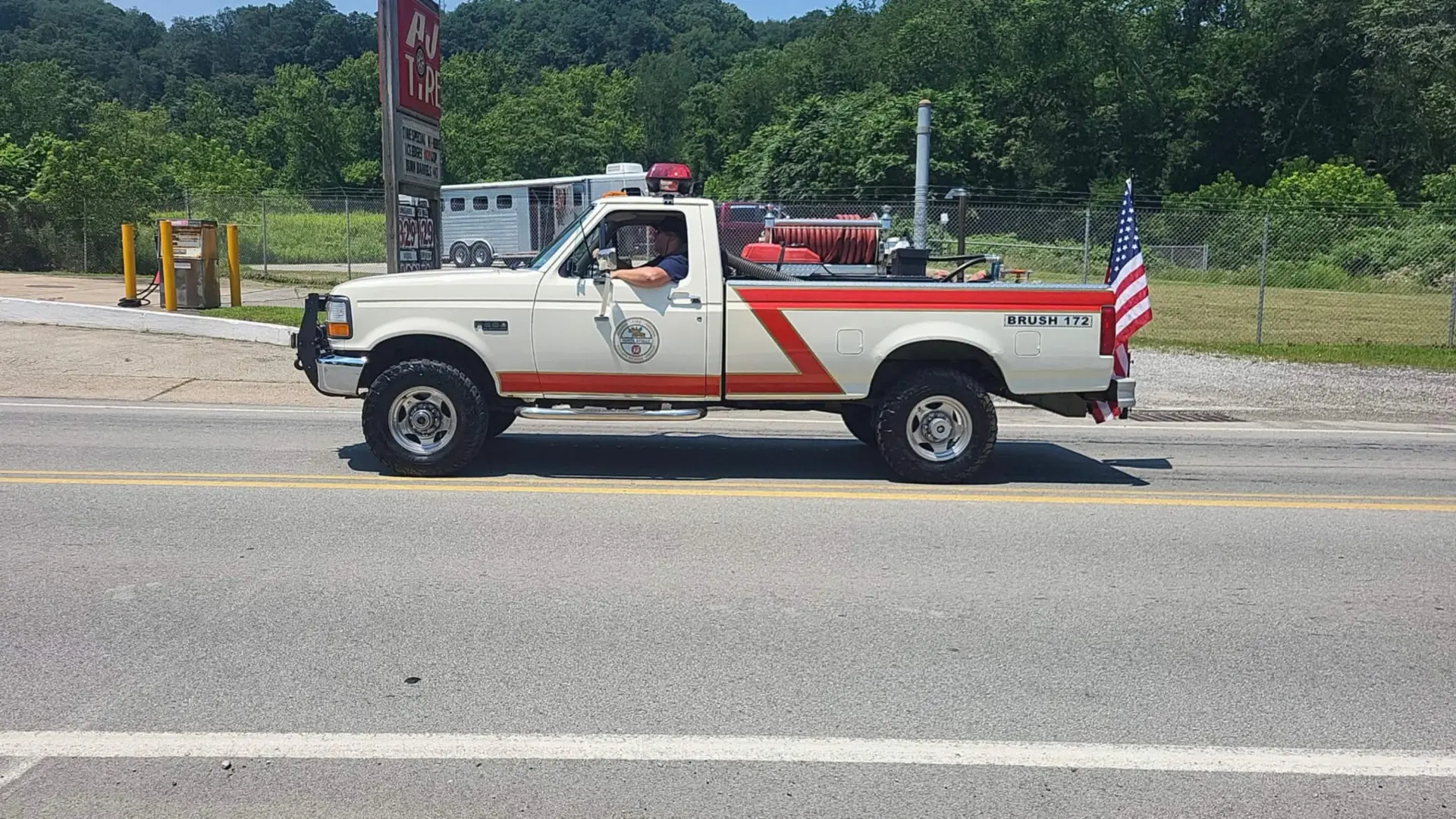 Brush 172 pickup with hose reel and American flag driving through town